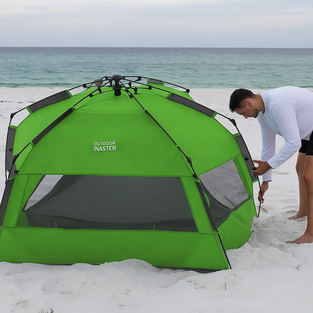 Man setting up a green pop-up tent on a sandy beach with calm ocean waves in the background.
