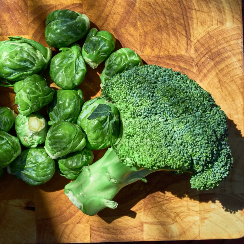 Fresh broccoli and Brussels sprouts on a wooden chopping board.