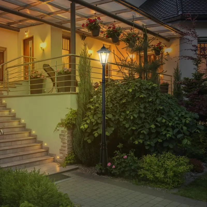 Residential lamp post illuminating a cozy porch with elegant landscaping at night.