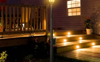 Illuminated outdoor lamp post beside wooden deck at night with glowing stair lights