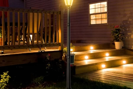 Illuminated outdoor lamp post beside wooden deck at night with glowing stair lights