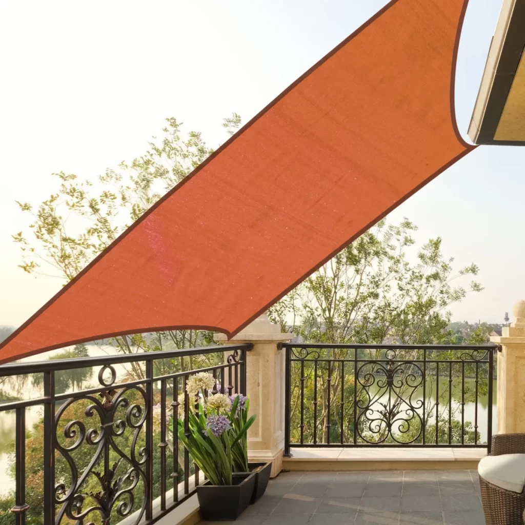 Red sun shade sail over a balcony garden with potted plants and railing.