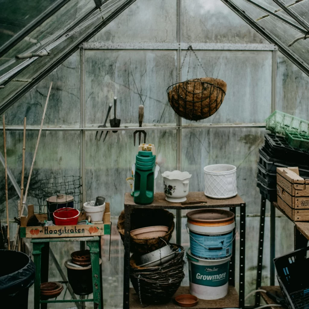 A cluttered greenhouse shelf filled with gardening tools and containers.