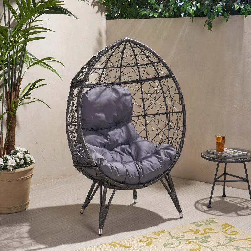 Modern egg-shaped outdoor chair with gray cushions beside side table and potted plants.