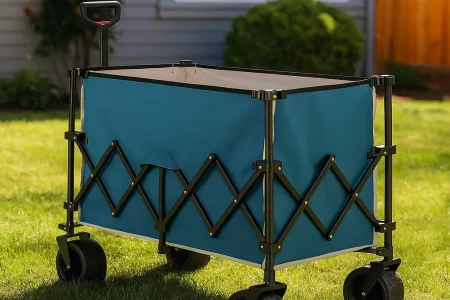 Compact folding wagon loaded with outdoor gear, parked on grass with trees in background.