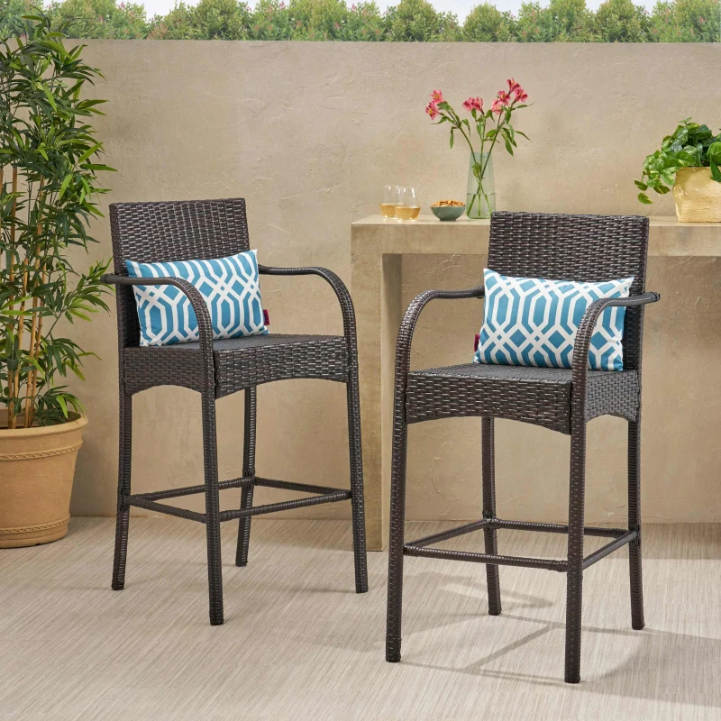 Outdoor wicker bar stools with armrests and patterned cushions beside a garden-themed bar.
