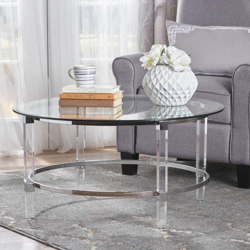 Glass coffee table with chrome legs styled with books, a vase, and a striped mug in a cozy room.

