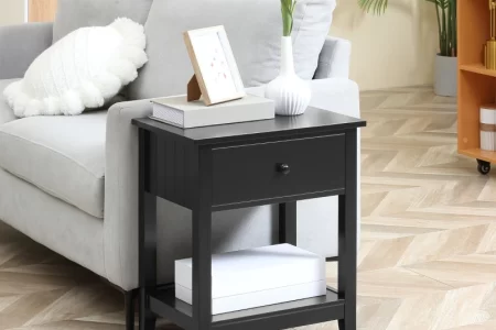 Black end table with drawer and lower shelf next to a gray sofa in a stylish living room.
