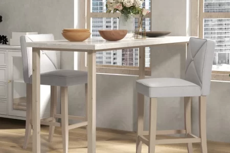 White bar table with two wooden bar stools in a modern, sunlit dining area.