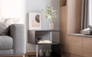 Modern black end table styled with books, a vase, and artwork beside a grey sofa.