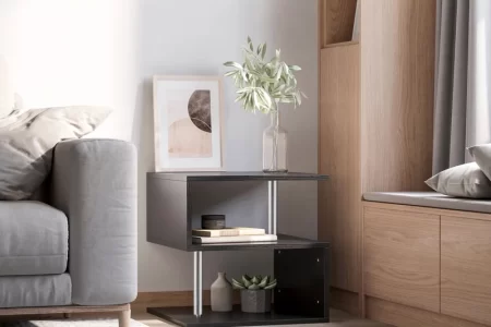 Modern black end table styled with books, a vase, and artwork beside a grey sofa.
