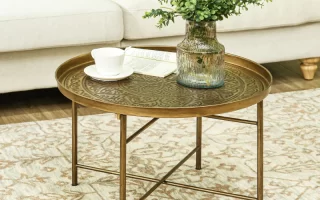 Brass round table styled with a textured glass vase, eucalyptus stems, coffee cup, and open book.