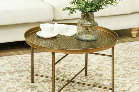 Brass round table styled with a textured glass vase, eucalyptus stems, coffee cup, and open book.