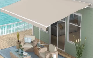 Beige retractable awning installed over coastal deck with wicker patio furniture and ocean view.