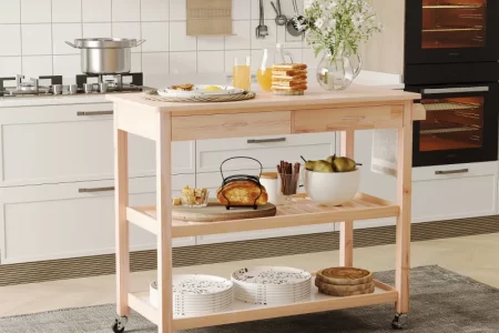 Light wood kitchen island cart with drawers and shelves styled for breakfast in a modern white kitchen.
