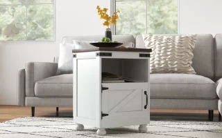 White farmhouse-style end table with open shelf and barn door, placed near grey sectional in bright room.