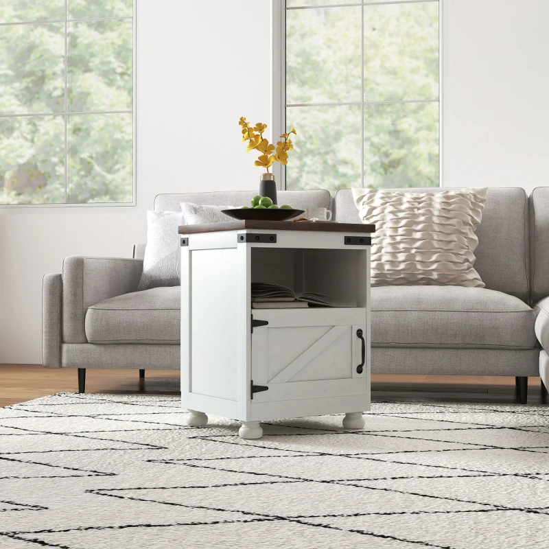 White farmhouse-style end table with open shelf and barn door, placed near grey sectional in bright room.
