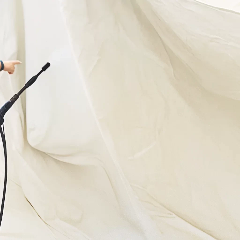 Person spraying water to moisten tent fabric during cleaning process under covered area.