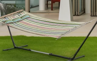 Fully assembled hammock on metal stand placed on green lawn outside a modern house.