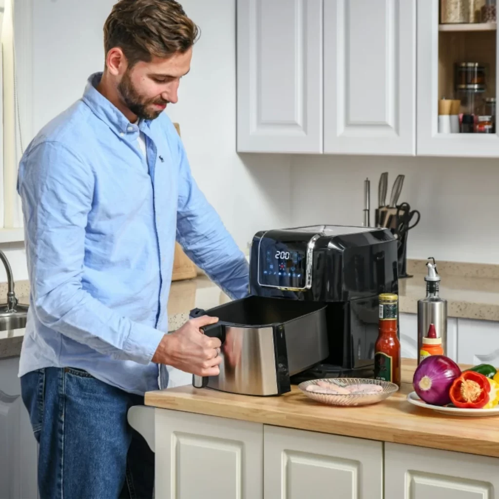 Man using black air fryer in modern kitchen with vegetables.