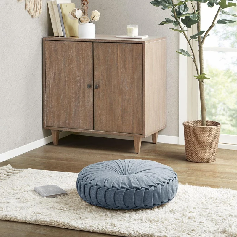 Blue round floor cushion placed on cream shaggy rug near cabinet.