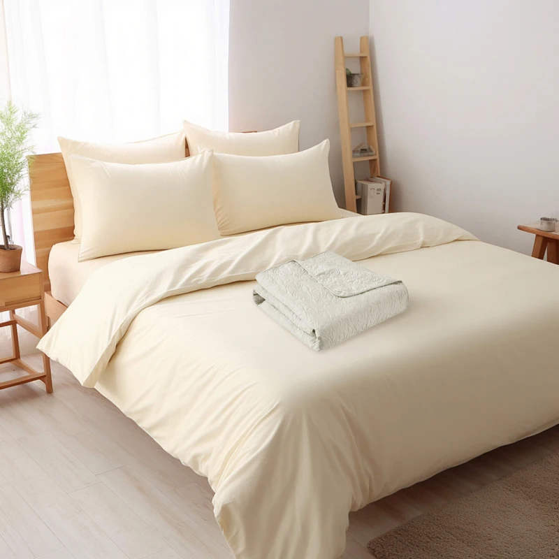 Bed with soft yellow bedding and a folded blanket. 