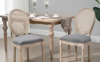 Natural wood oval-back dining chairs with grey cushions around a rustic farmhouse table in a bright dining room.
