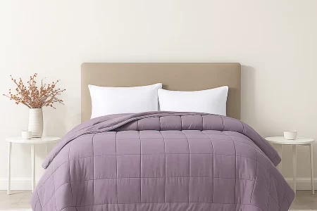 Lavender quilted comforter on bed with beige headboard and white pillows.