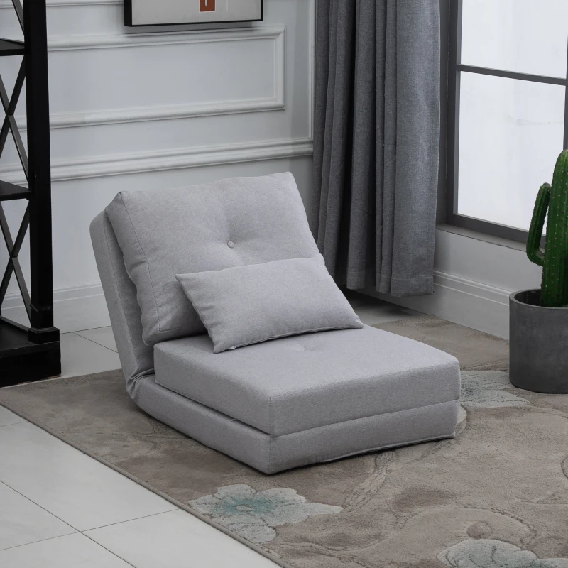 Compact light grey futon chair with pillow, placed on floral rug near grey curtain and cactus plant.
