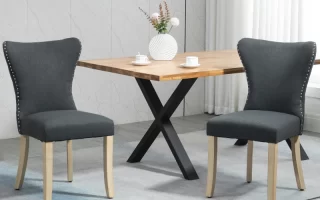 Pair of dark grey fabric dining chairs with nailhead trim placed around a wooden dining table.