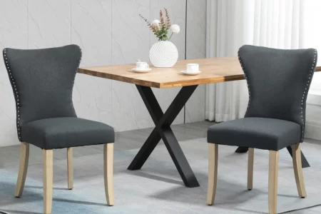 Pair of dark grey fabric dining chairs with nailhead trim placed around a wooden dining table.