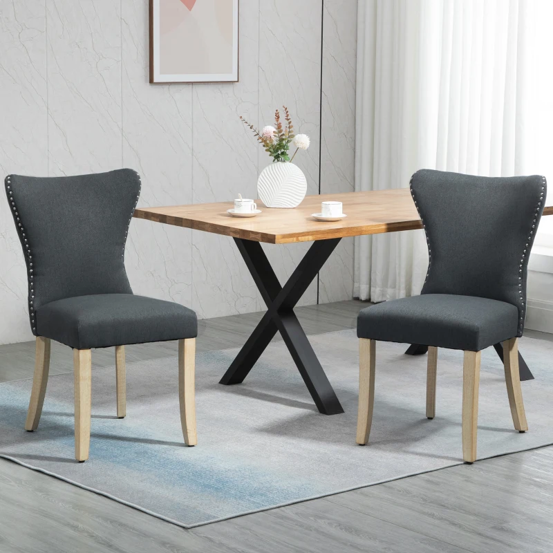 Pair of dark grey fabric dining chairs with nailhead trim placed around a wooden dining table.