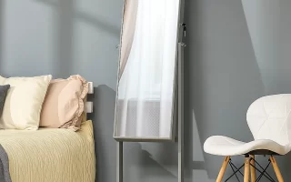 Clean, full-length bedroom mirror beside bed and white chair.