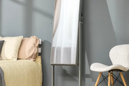 Clean, full-length bedroom mirror beside bed and white chair.