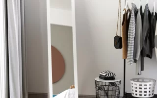 Minimalist full-length mirror in modern bedroom beside clothes rack.