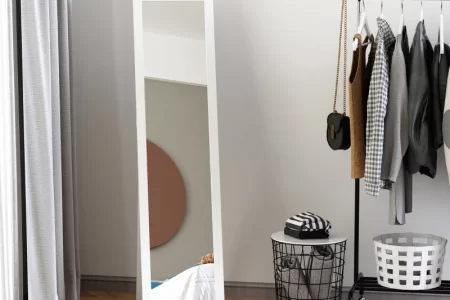 Minimalist full-length mirror in modern bedroom beside clothes rack.