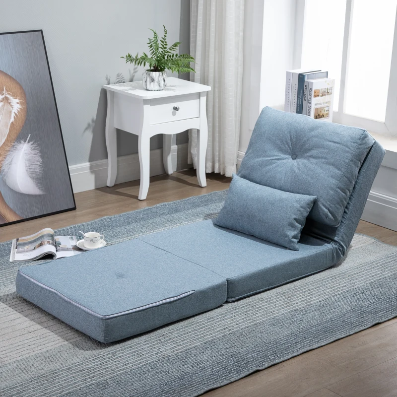 Light blue foldable futon mattress laid flat on striped rug with pillow and side table near window.
