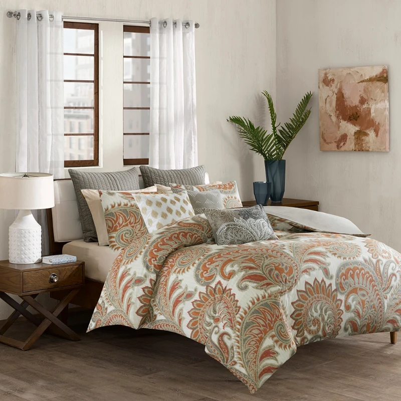 Bedroom with patterned bedding set, multiple cushions, and nightstand lamp.