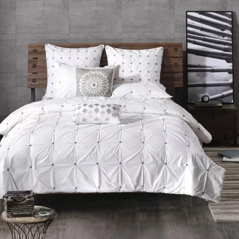 Modern bedroom with white tufted bedding and decorative grey cushions.