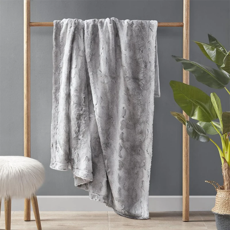 Cozy grey throw blanket hanging on wooden rack.