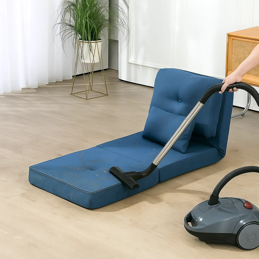 Hand vacuuming dirt from blue futon cushion on floor


