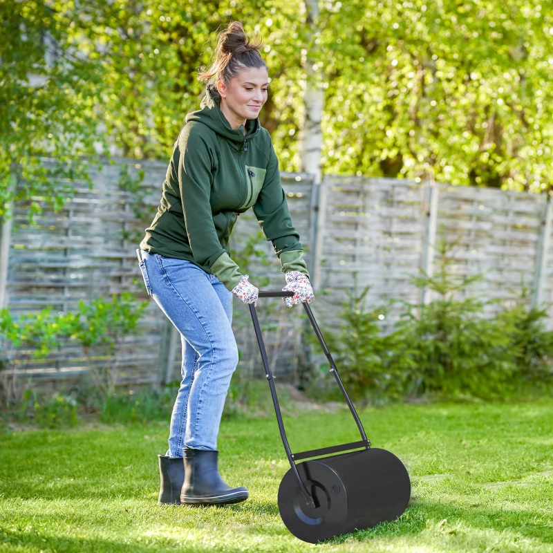 Person using a black steel lawn roller on a bright green lawn.