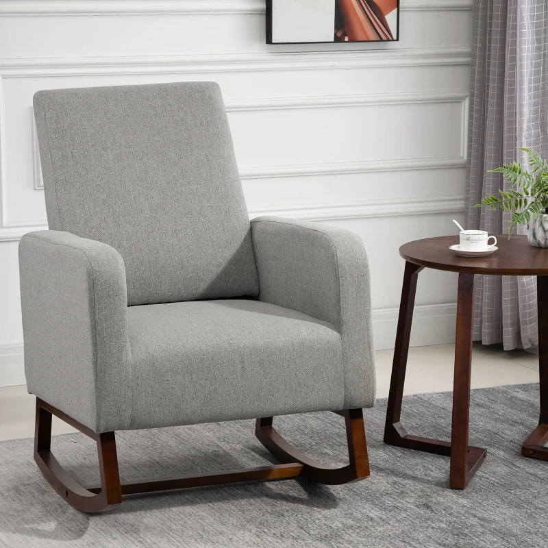 Grey fabric rocking chair with wooden legs beside round table.
