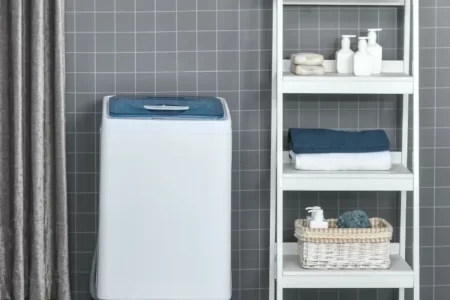 Compact washing machine placed beside storage cabinet and laundry basket