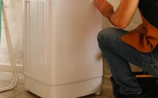 Man kneeling beside washing machine with repair tools on floor