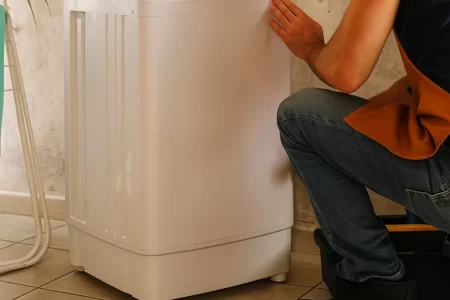 Man kneeling beside washing machine with repair tools on floor