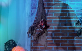 Creepy bat prop hanging outdoors with cobwebs and pumpkin lights.