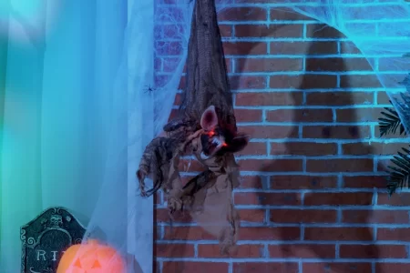 Creepy bat prop hanging outdoors with cobwebs and pumpkin lights.