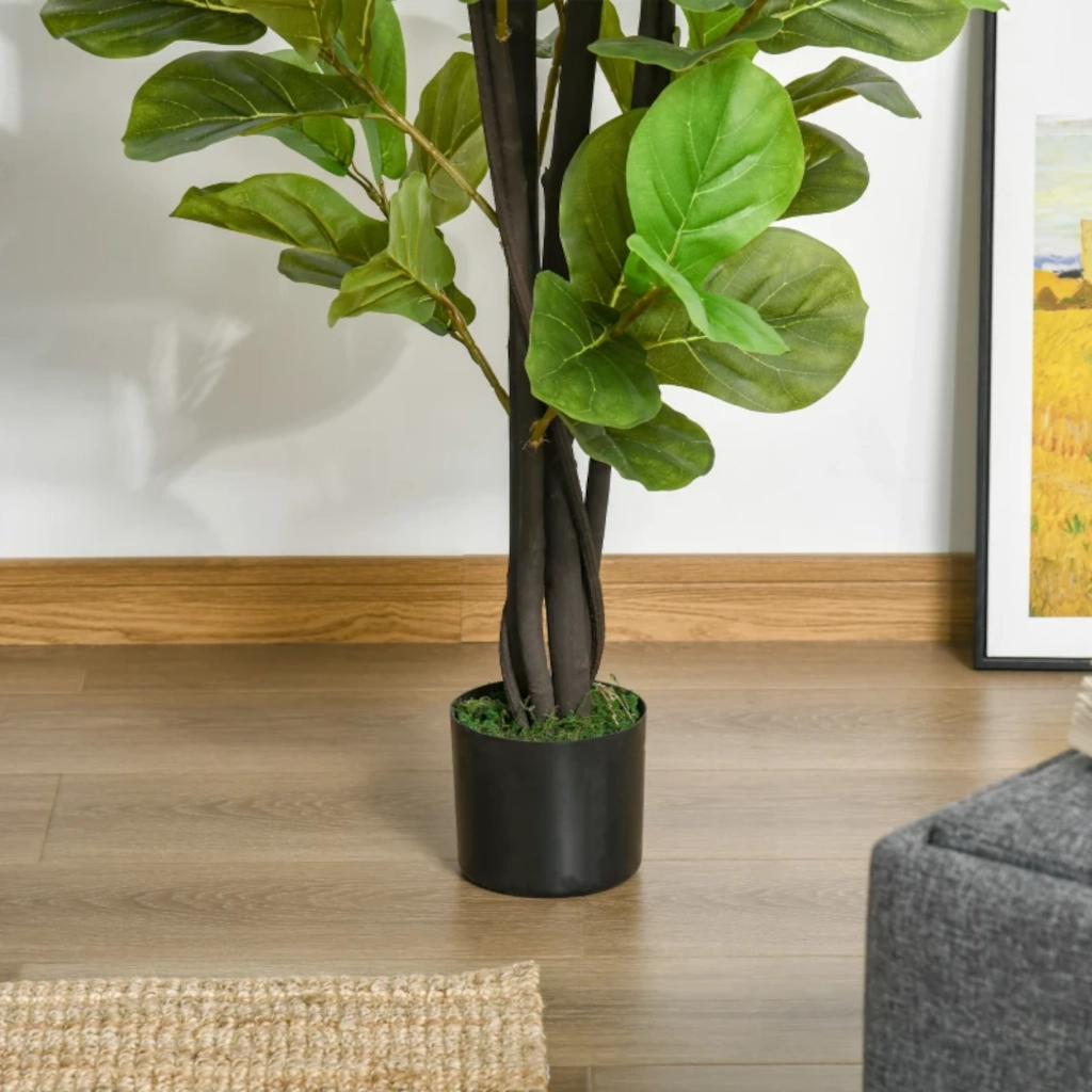 Tall faux tree in black nursery pot beside wall and framed art on wooden floor.
