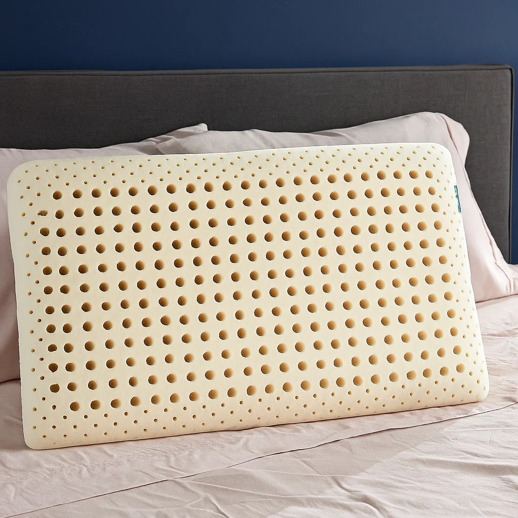 Perforated latex pillow resting on bed with gray headboard